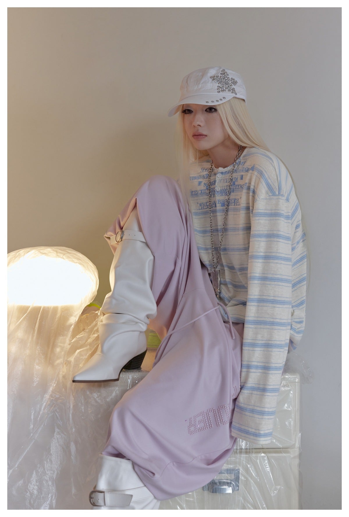 Model seated with one knee raised, wearing a cream-and-blue striped top and lavender pants.