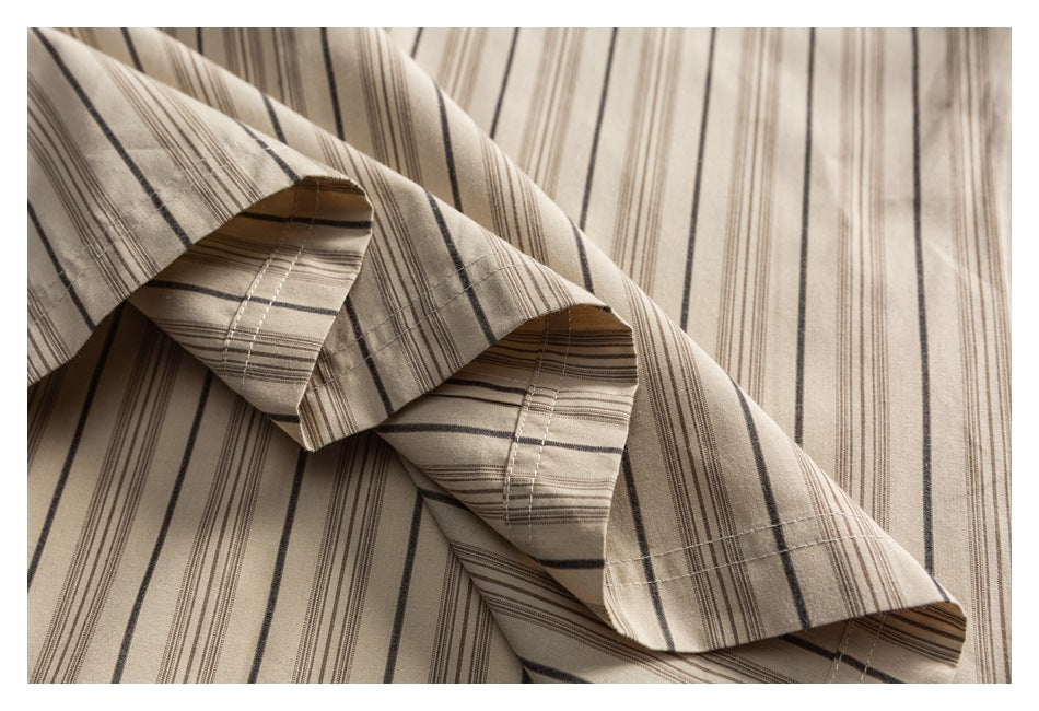 Close-up of folded beige striped shirt fabric showing a stitched edge and layered folds.