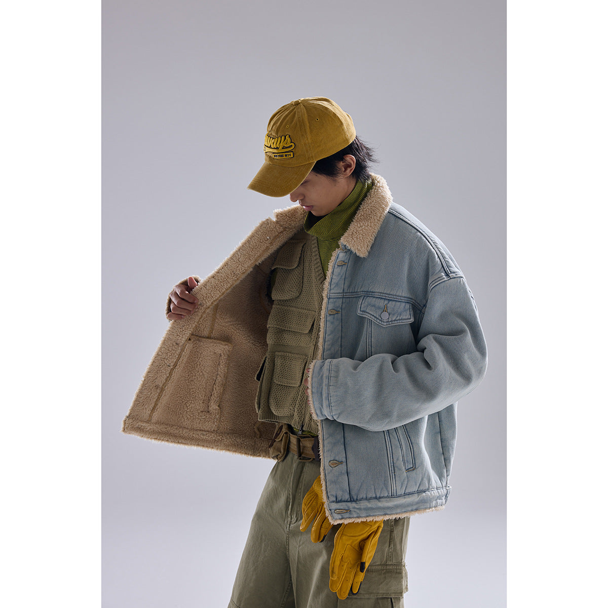 Model opens a light blue denim jacket to show its thick cream sherpa lining and interior pocket.