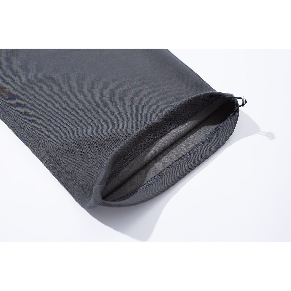 Close-up of a charcoal pant leg hem with stitching and a small metal adjuster.