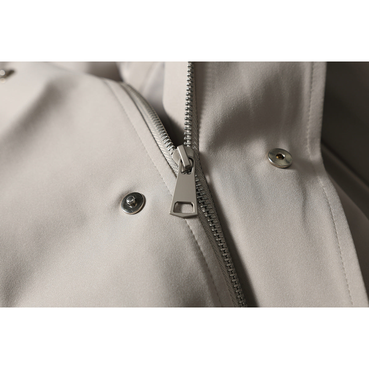 Close-up of the light taupe jacket’s metal front zipper and snap fasteners.