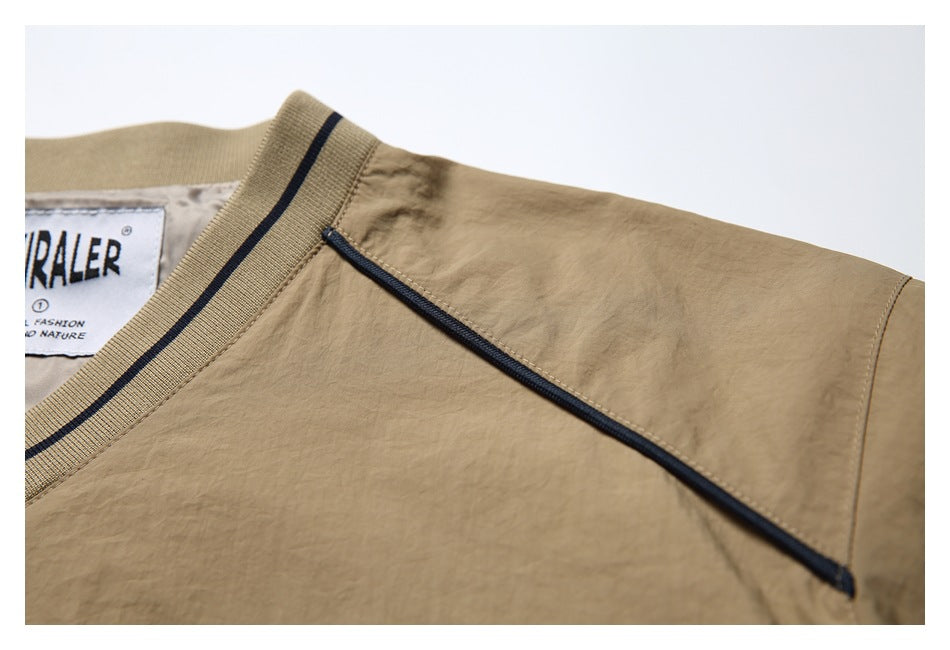 Close-up of a tan garment's shoulder seam and diagonal navy-trimmed zip pocket.