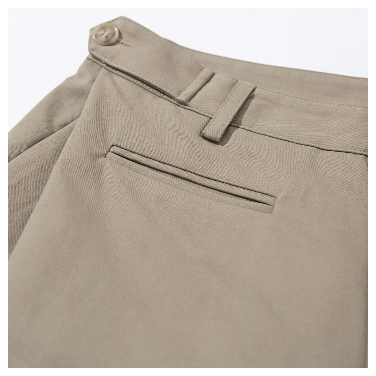 Angled close-up of taupe trousers with a waistband button, belt loops and a narrow welt pocket.