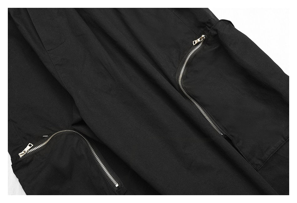 Close-up of black pants showing two curved pockets with silver zippers.