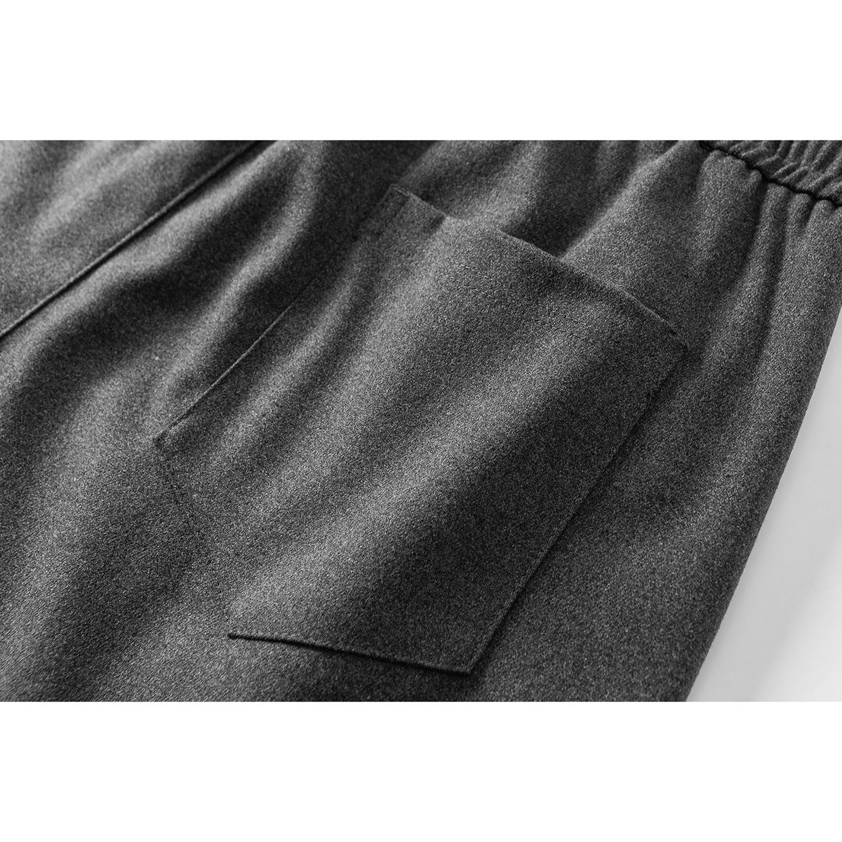 Close-up of charcoal gray pants showing a rectangular side pocket and part of the elastic waistband.