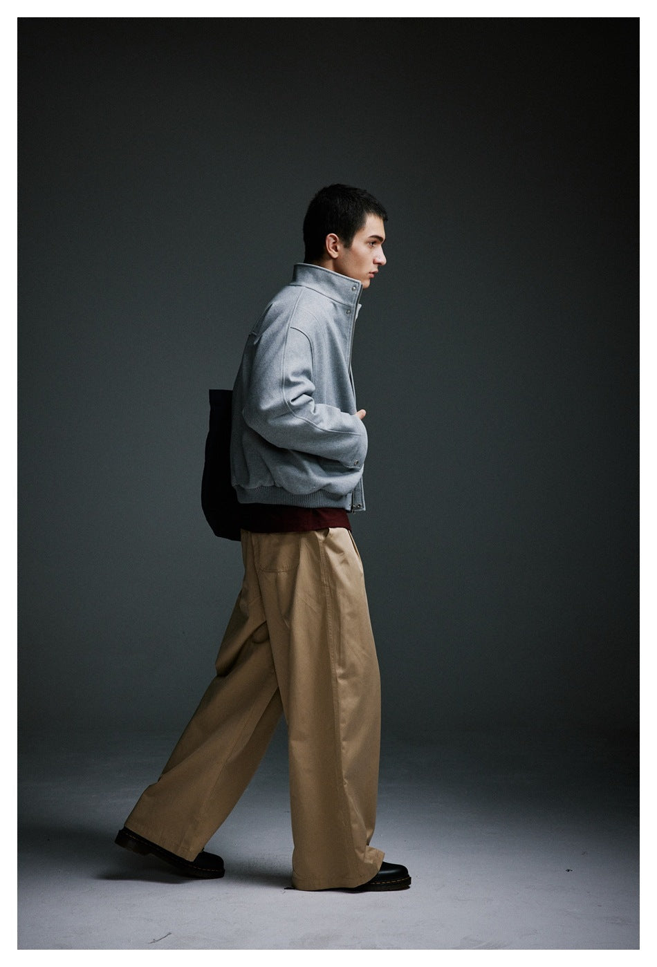 Side view of a model wearing a light gray jacket with a raised collar and wide tan trousers.