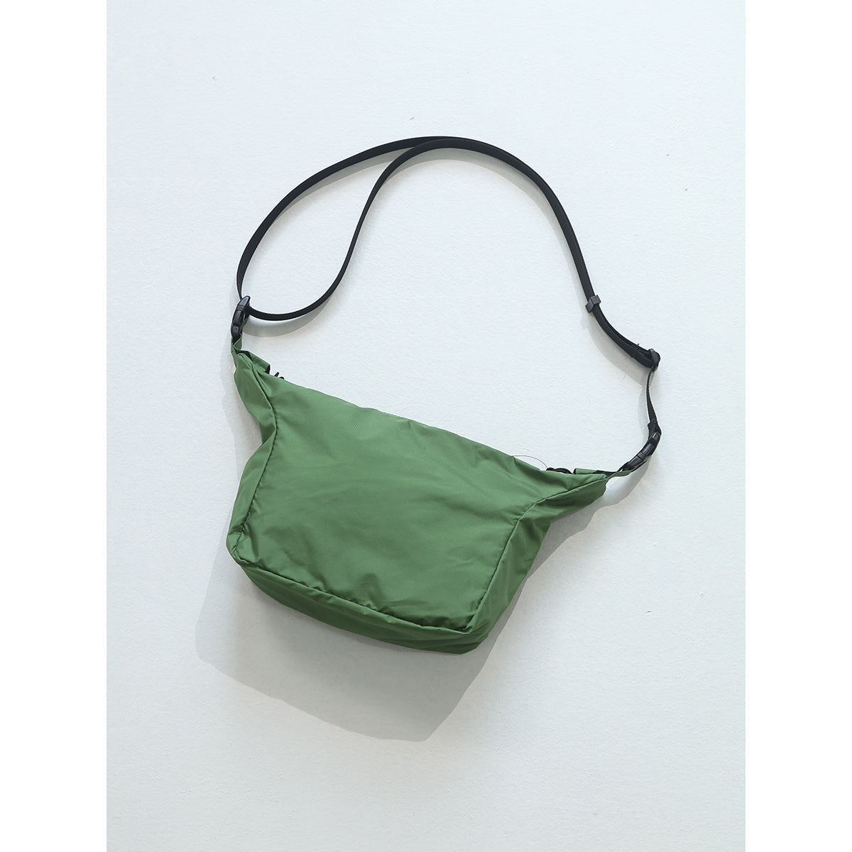 Green crossbody bag with black adjustable strap and side-release buckles on a light background