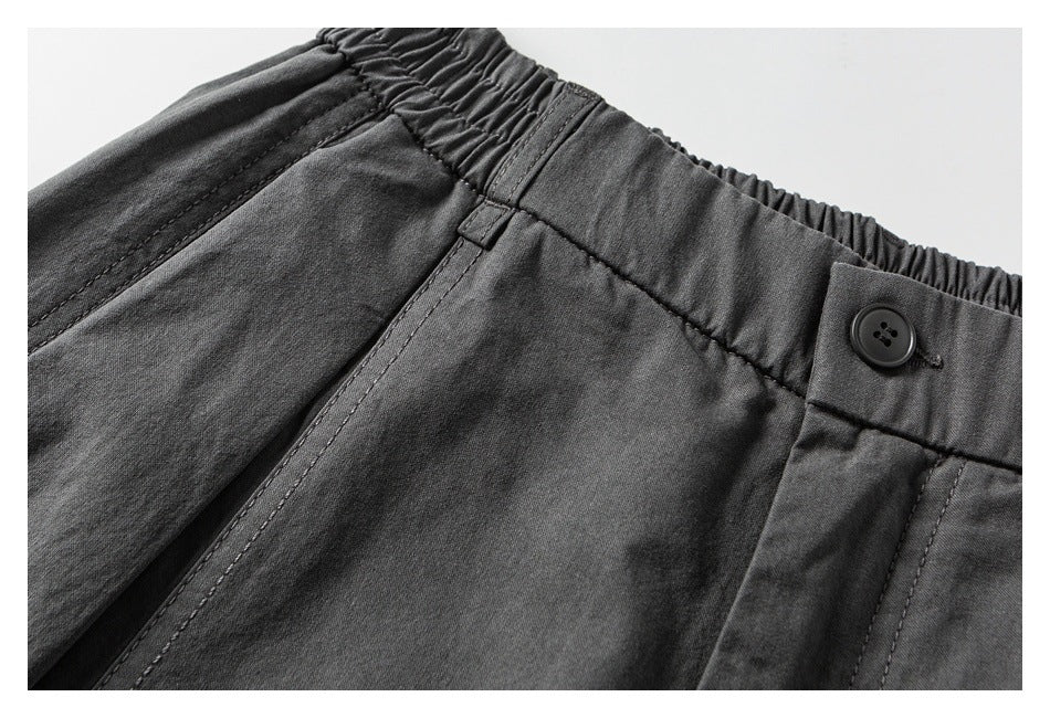 Close-up of charcoal pants showing the elasticated waist, button, belt loop, and front seam.