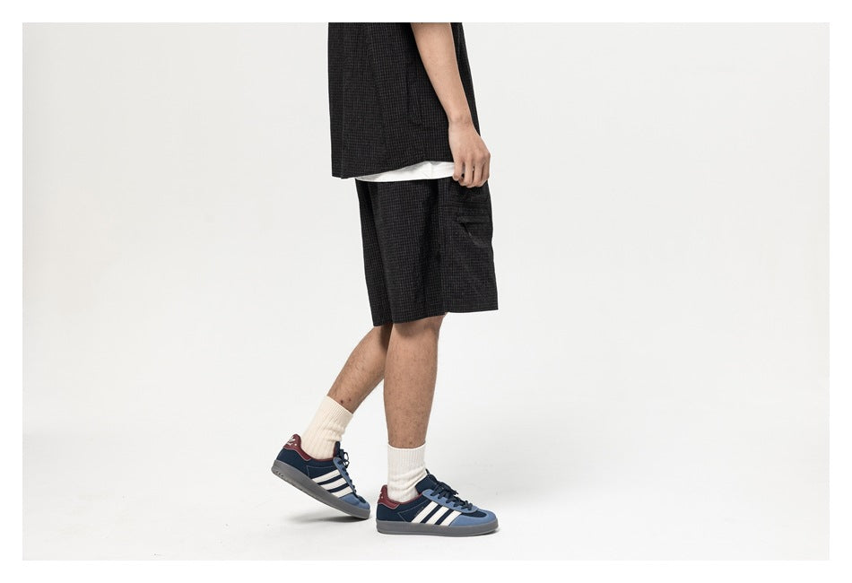 Side view of a person wearing black check shorts, white socks, and blue sneakers.