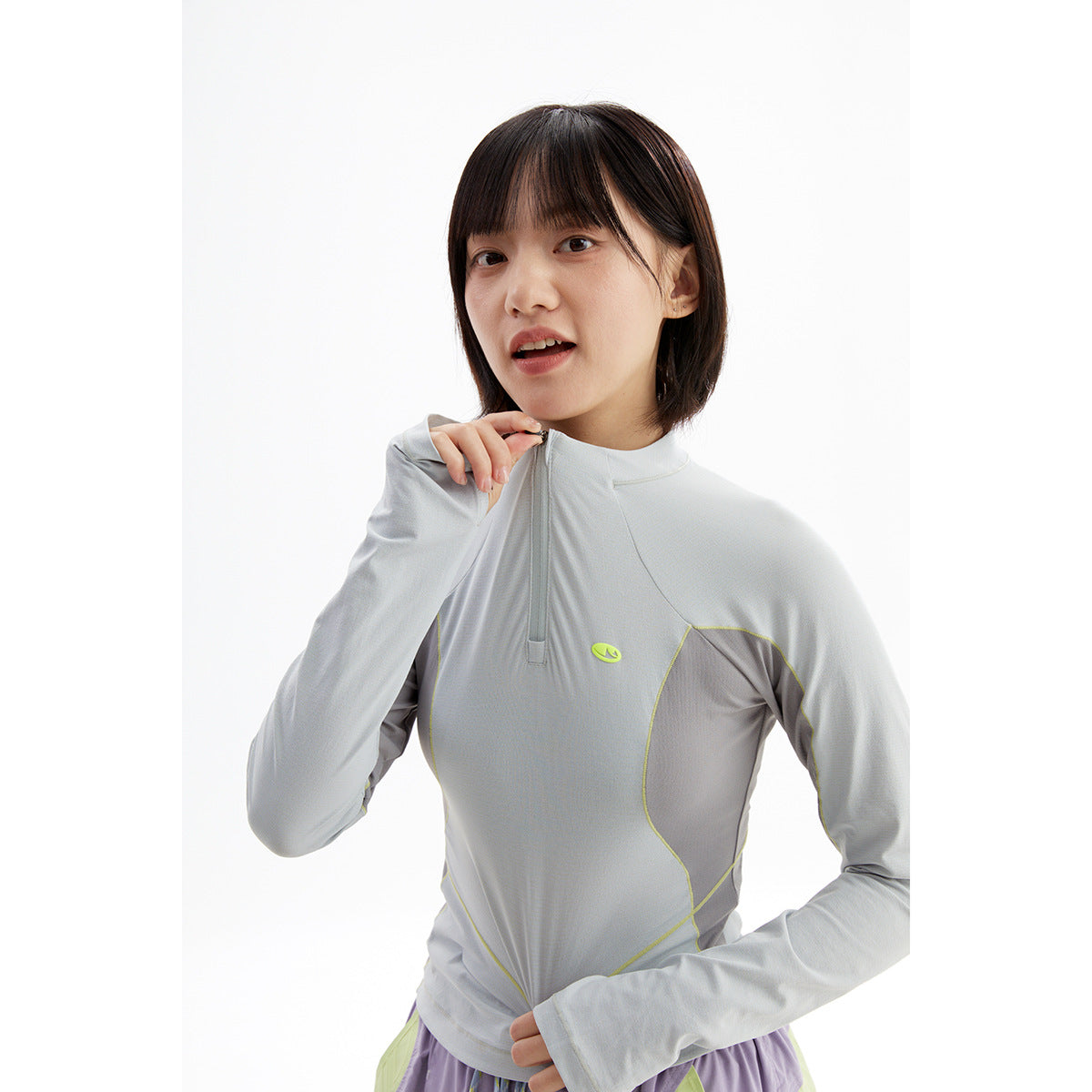 Close view of a model wearing a light gray quarter-zip top with lime piping and darker gray panels.