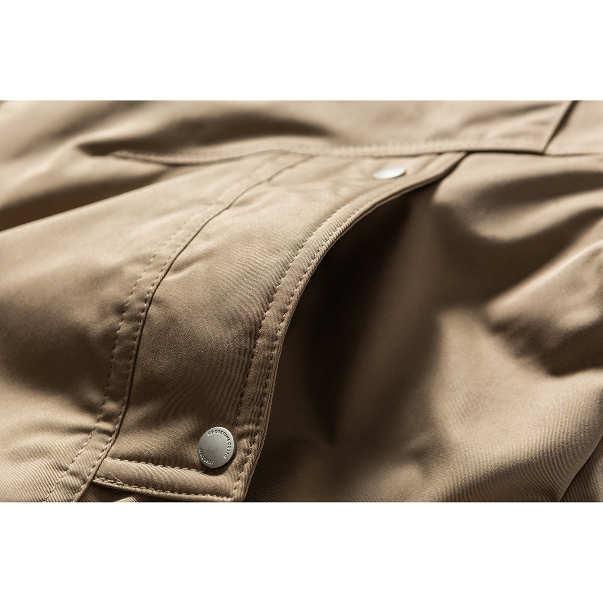 Close-up of tan jacket fabric, stitched placket, and metal snap fasteners.