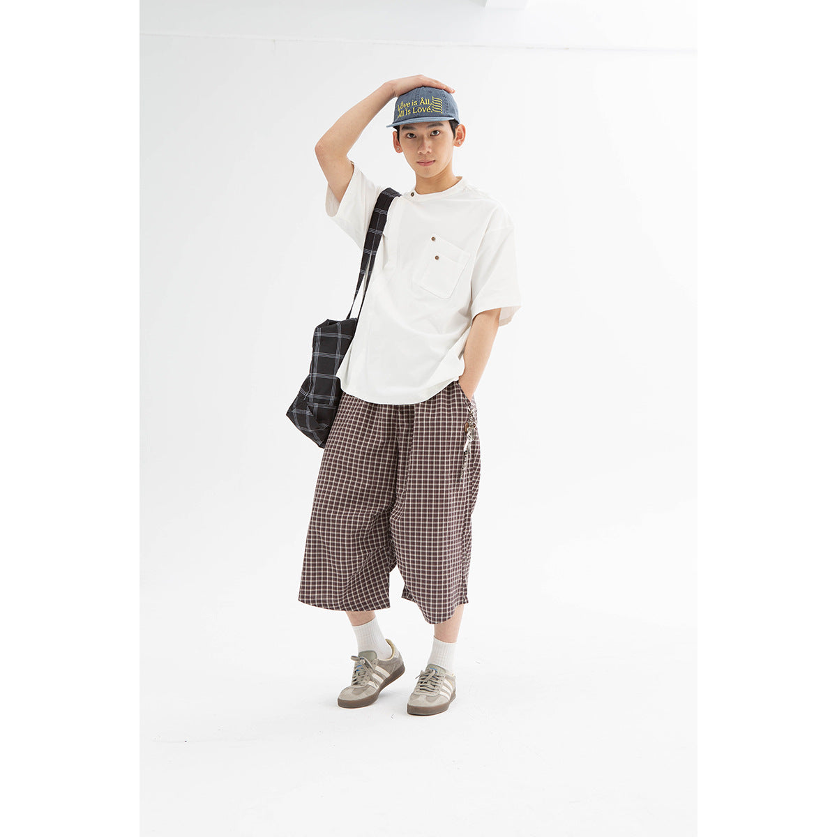 Model wearing a white pocket T-shirt and loose brown plaid shorts, front view.
