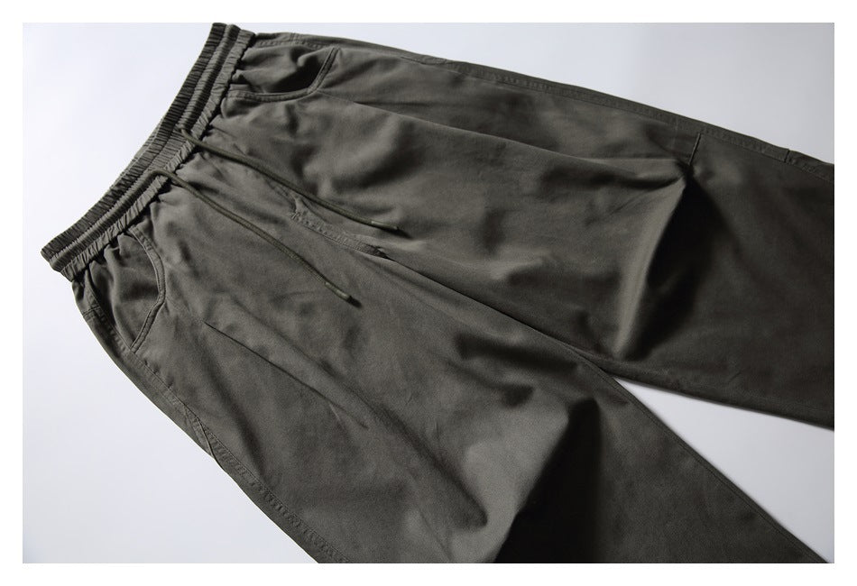Dark olive pants laid flat at an angle, showing the elastic drawstring waist, front pockets, and relaxed legs.