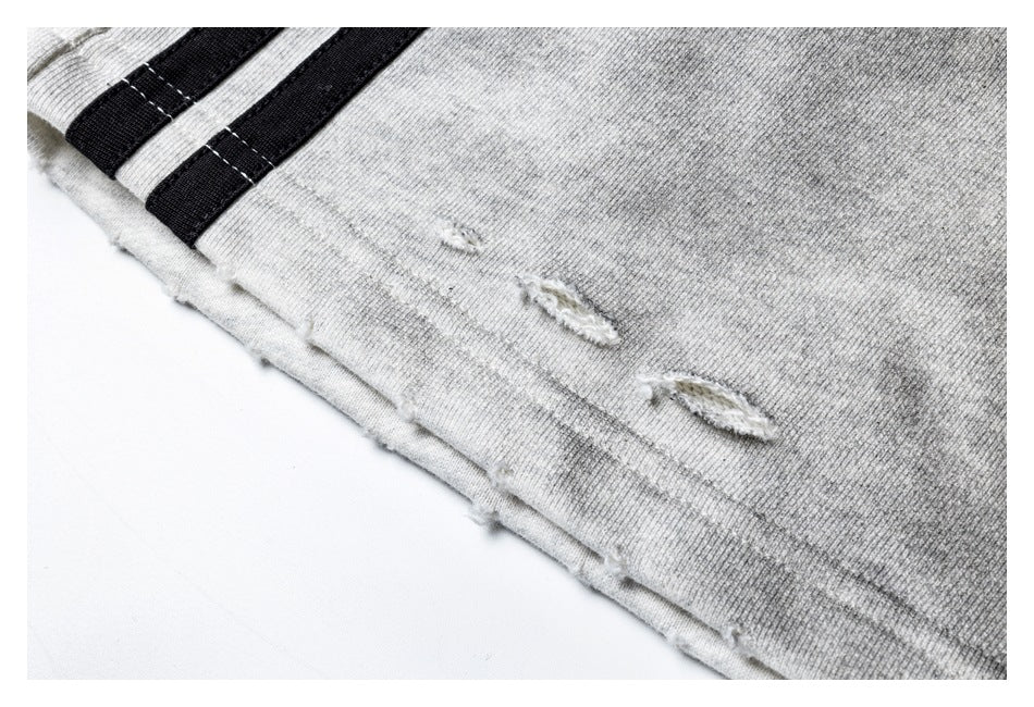 Close-up of a distressed hem on light gray shorts with two black side stripes.
