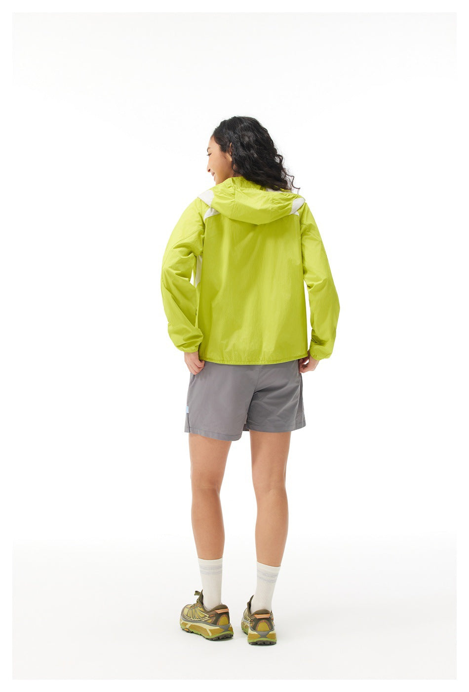 Rear view of model in a lime hooded jacket and gray shorts, showing the jacket's back and hood.