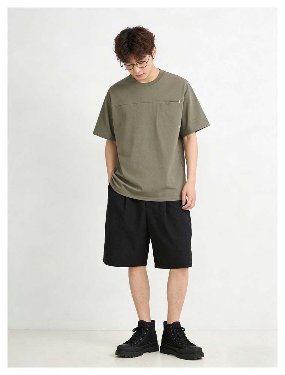 Model wearing an olive short-sleeve T-shirt with a horizontal chest seam and black shorts, front view.