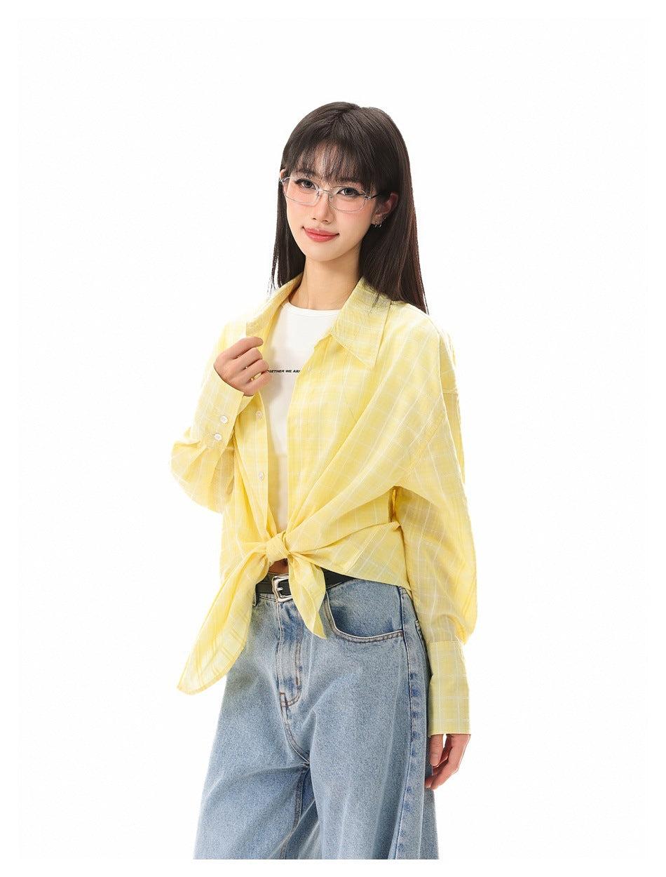 Model wearing a yellow-and-white plaid shirt tied at the waist over a white tee and blue jeans.