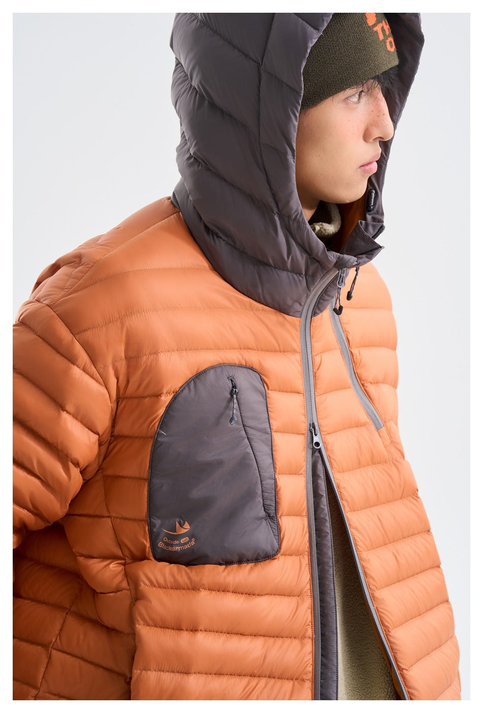 Close-up of an orange quilted puffer jacket with a gray hood, zipper trim, and chest pocket.