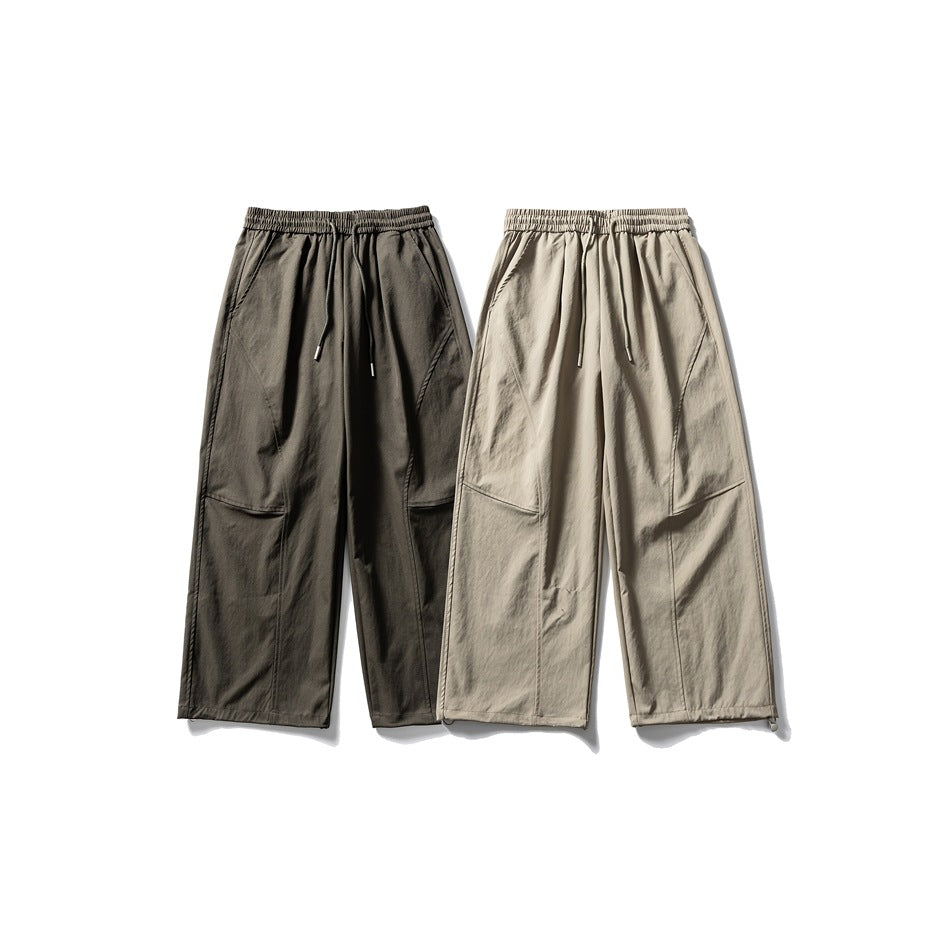 Two pairs of loose-fit pants in dark charcoal and beige, shown front-facing with elastic waists and panel details.