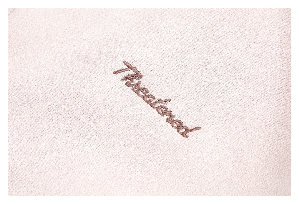 Close-up of embroidered brown script on pale pink garment fabric.