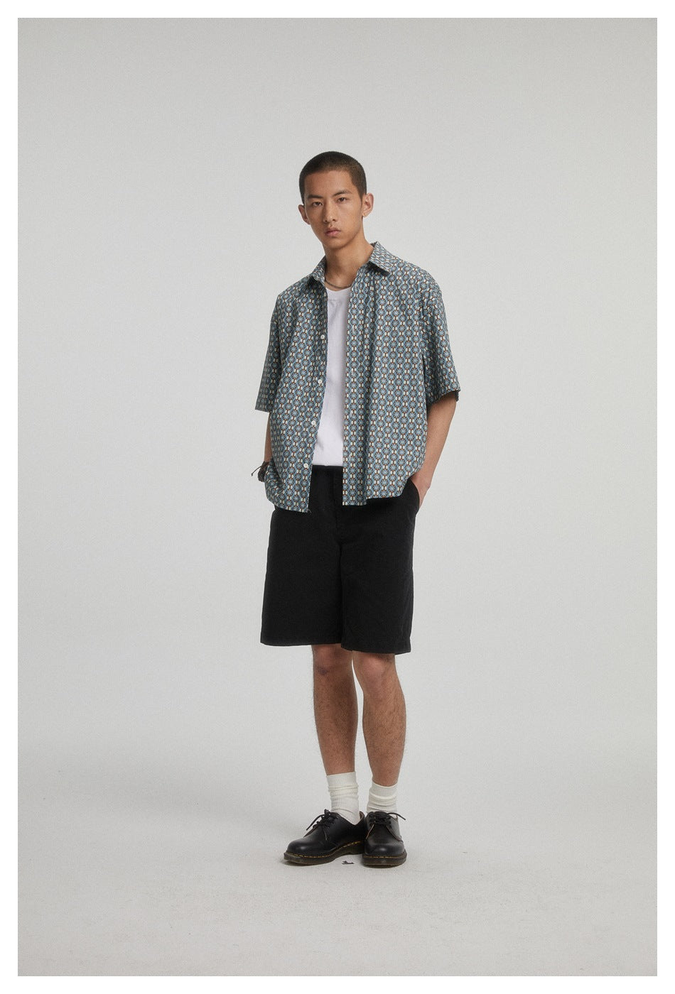 Model wearing a blue short-sleeve button-up shirt with a repeating floral pattern, white tee, and black shorts.