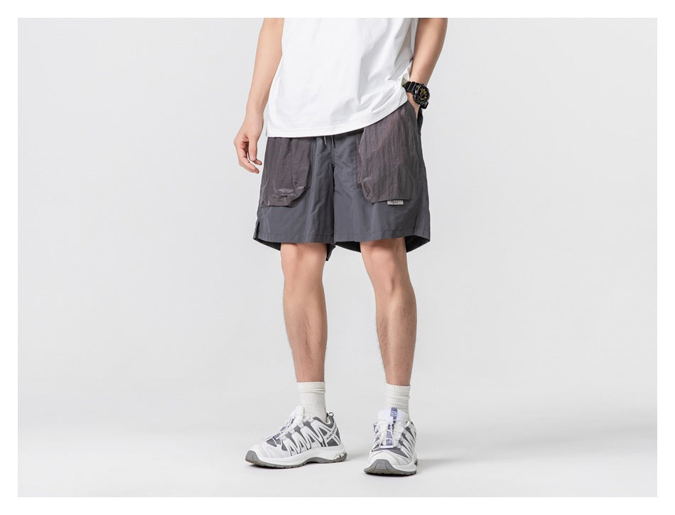 Front view of a model wearing dark charcoal shorts with large gray flap pockets against a plain studio background.