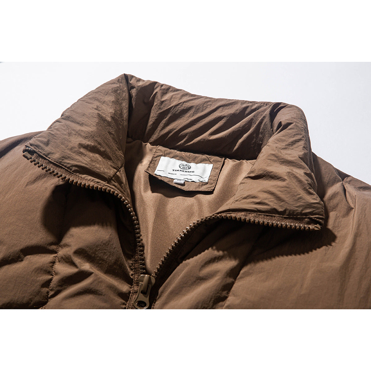 Close-up of a brown padded jacket's collar, front zipper, and sewn white neck label.