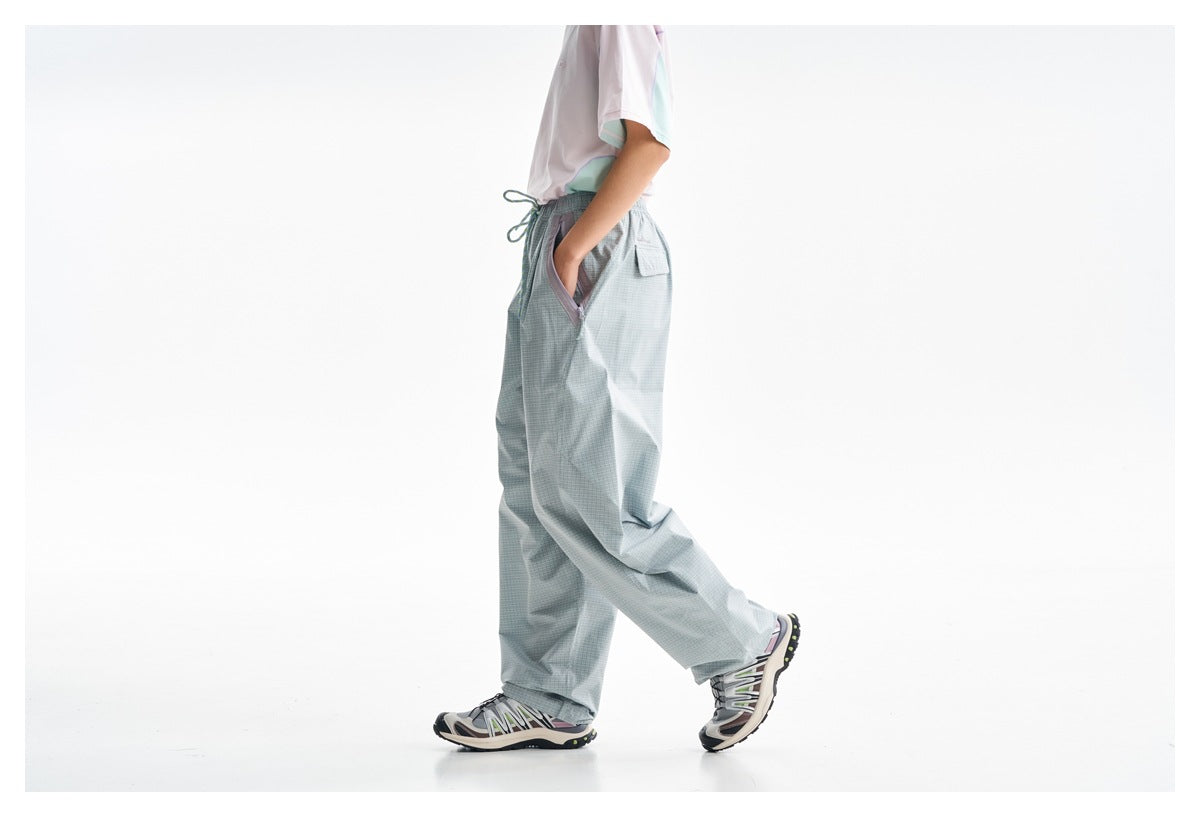 Side view of a model wearing loose pale blue-gray check trousers with a drawstring waist and contrast-trimmed pocket.