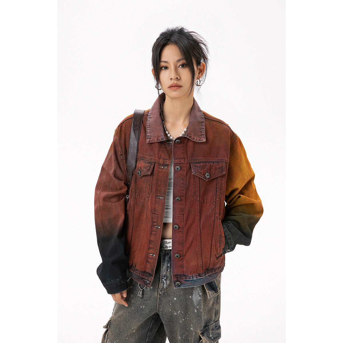 Model wearing a rust-red washed denim jacket with contrasting dark and ochre sleeves, front pockets and button closure.