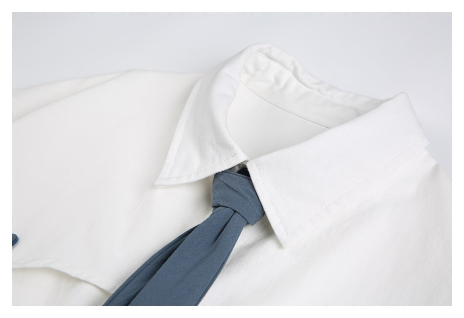 Close-up of a white collared garment with a slate-blue tie tucked beneath the collar.