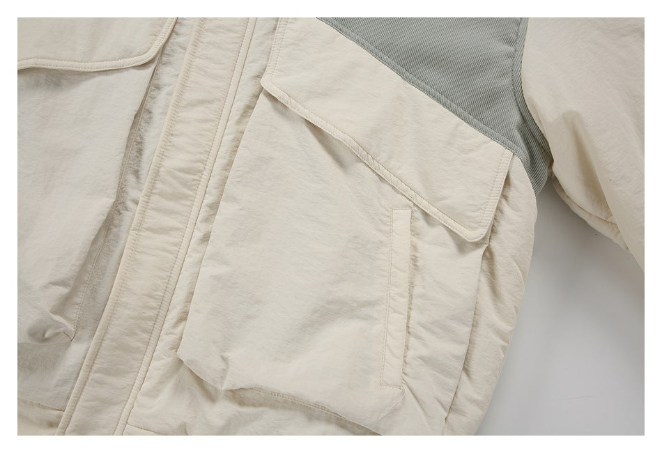 Close-up of a cream jacket flap pocket with gray upper panel and a vertical pocket opening.