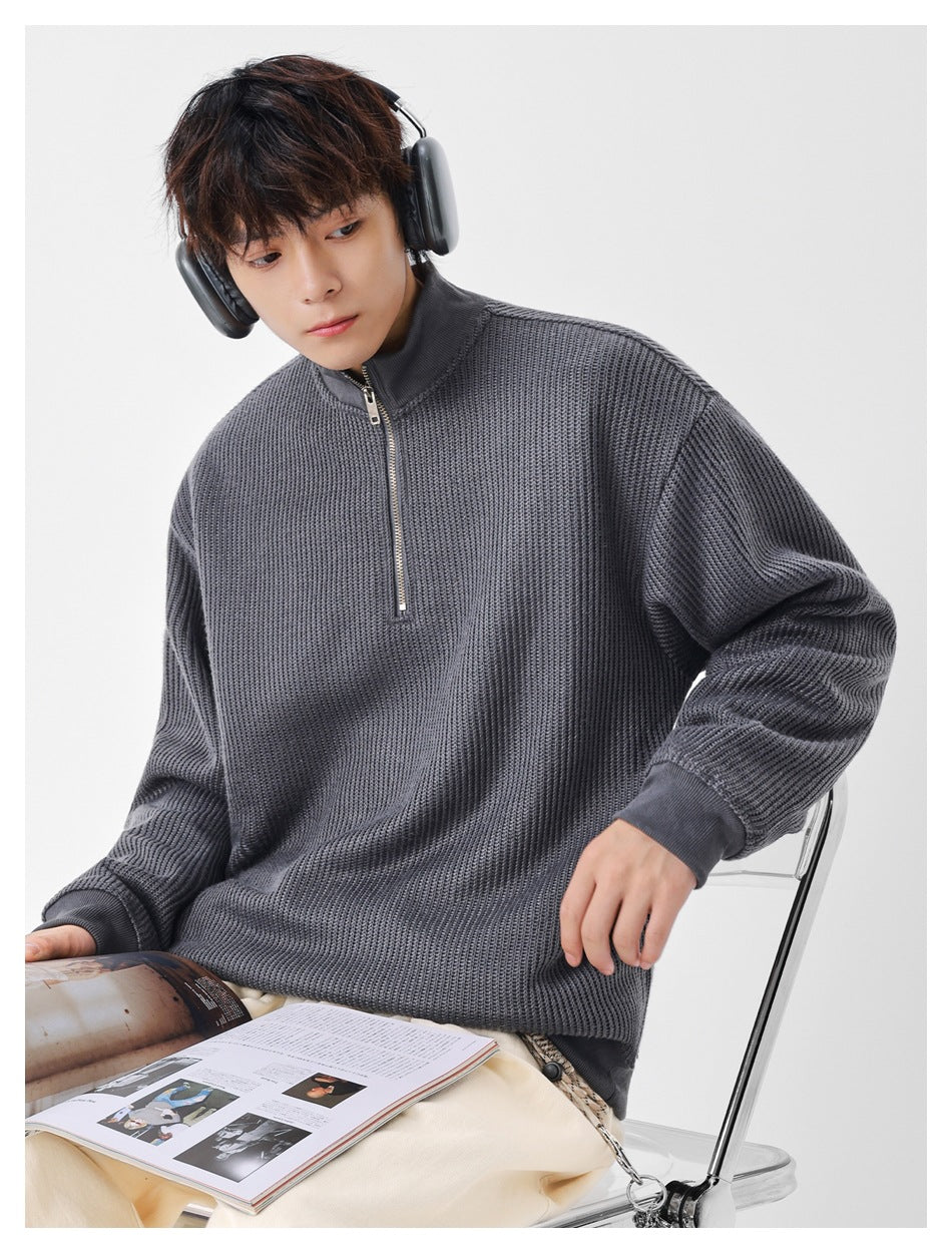 Model seated wearing an oversized charcoal gray textured quarter-zip sweater with a high collar and ribbed cuffs.