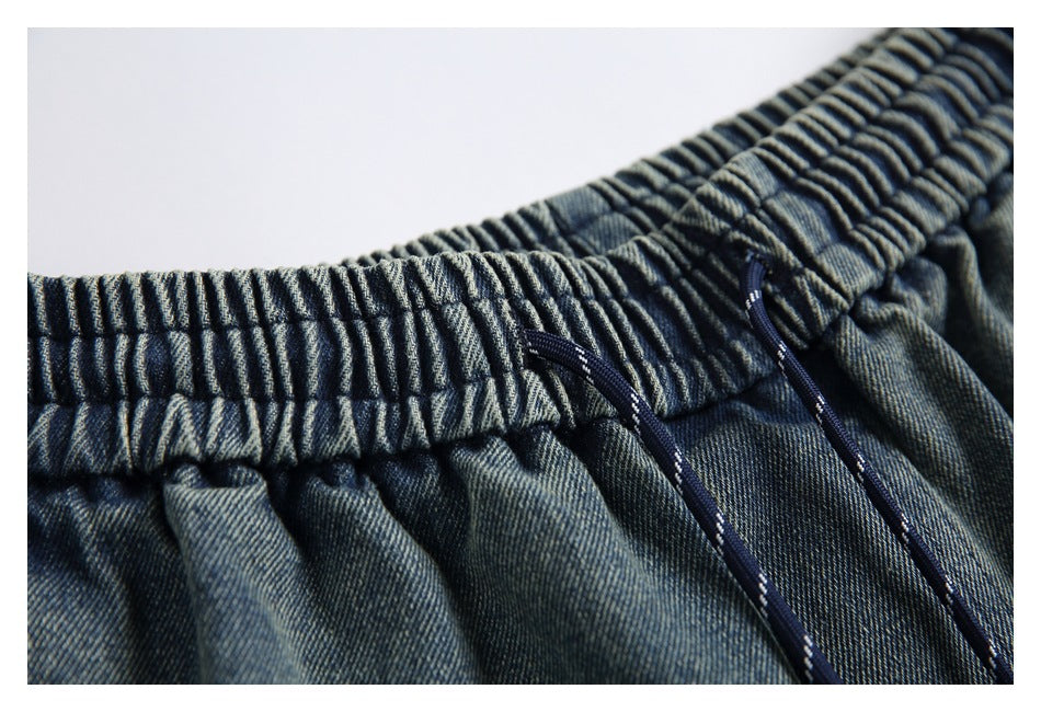 Close-up of the gathered elastic waistband and navy drawstrings on blue denim pants.