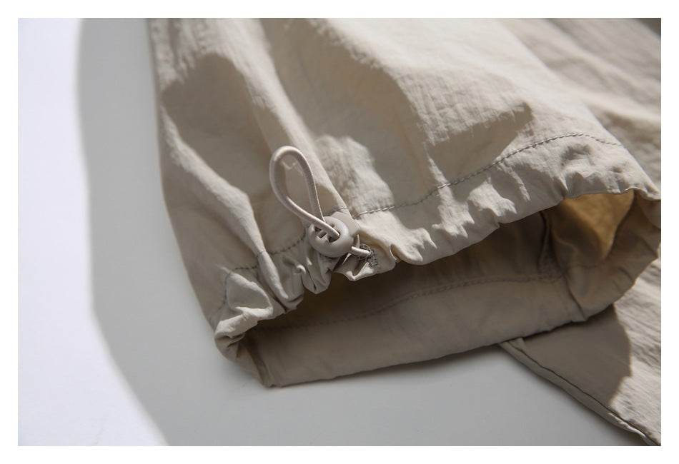 Close-up of a beige jacket hem with gathered fabric and an adjustable elastic drawcord toggle.