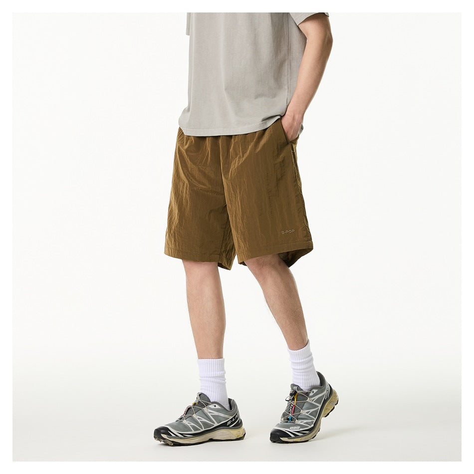 Angled view of a model wearing loose olive-brown knee-length shorts with a drawstring and pockets.