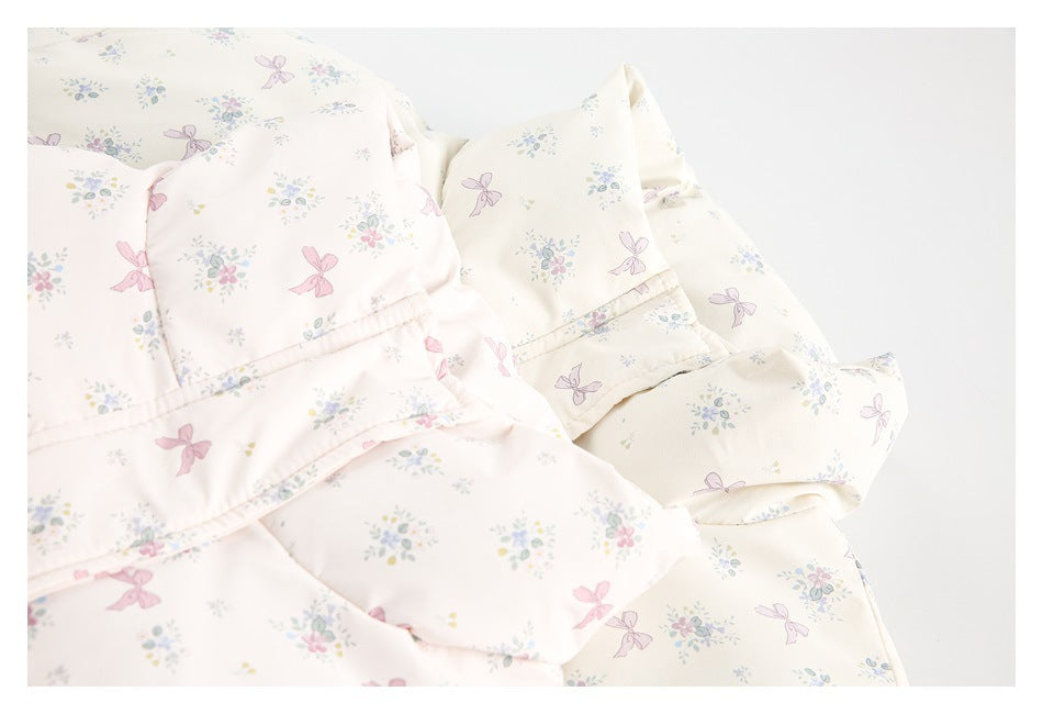 Close-up of pale pink and ivory garments with small floral and pink bow prints and piped edges.