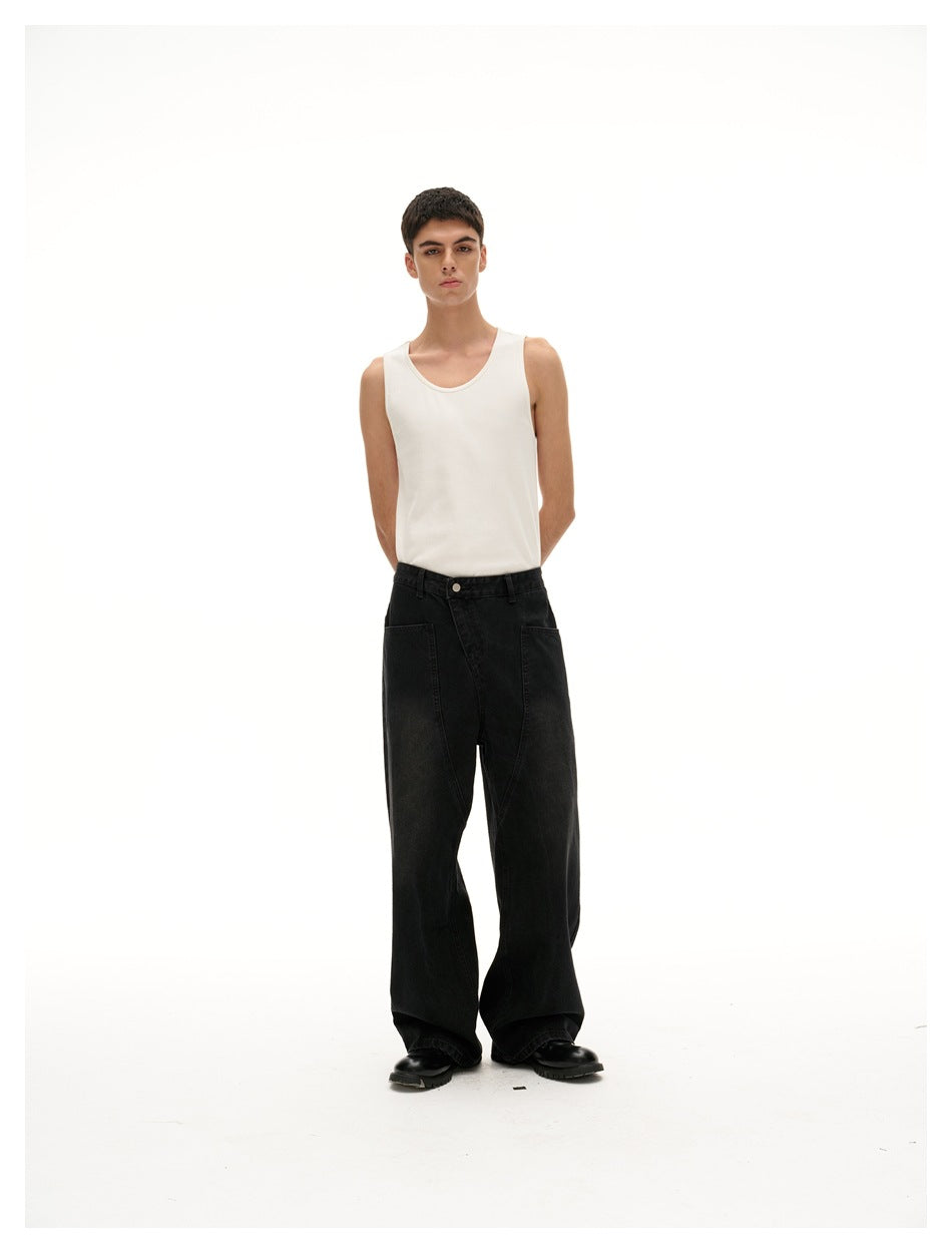 Model standing with hands behind his back, wearing a white tank top and wide black jeans.
