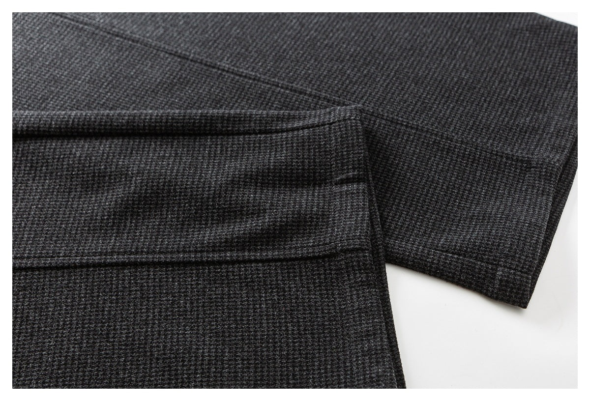 Close-up of dark charcoal patterned trousers showing a stitched edge and folded hem.