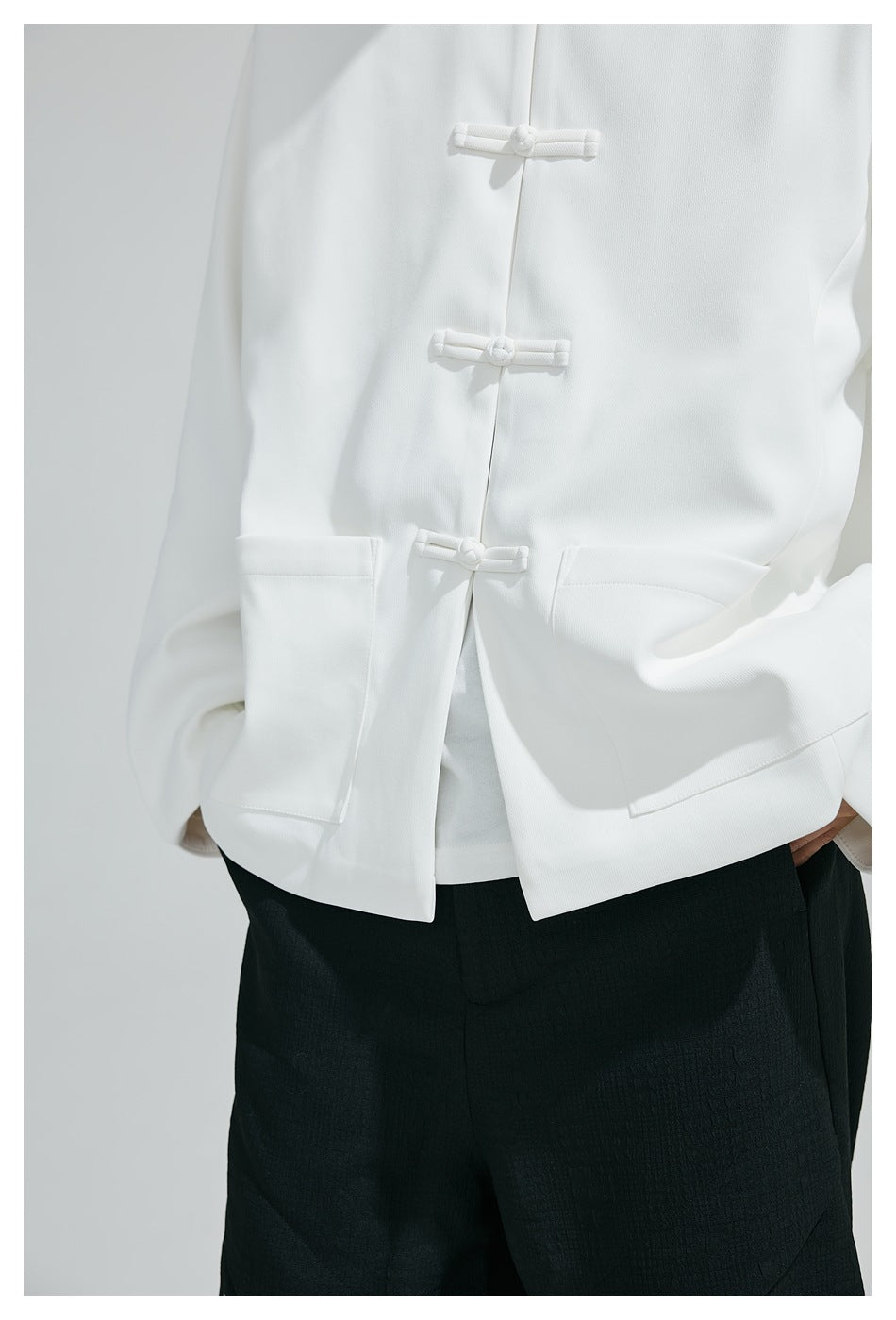 Close-up of a white jacket showing its frog closures, front opening, and large patch pockets.
