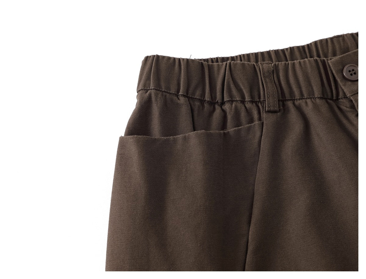 Close-up of dark brown trousers showing the elastic waistband, belt loop, button and angled pocket opening.