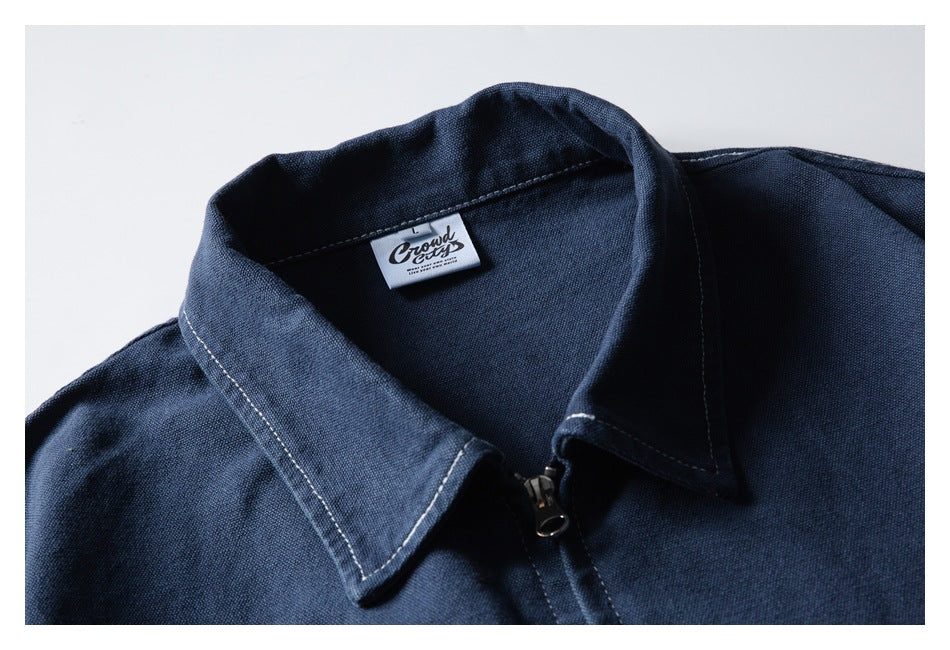 Close-up of a navy jacket's pointed collar, zipper, contrast stitching, and sewn neck label.