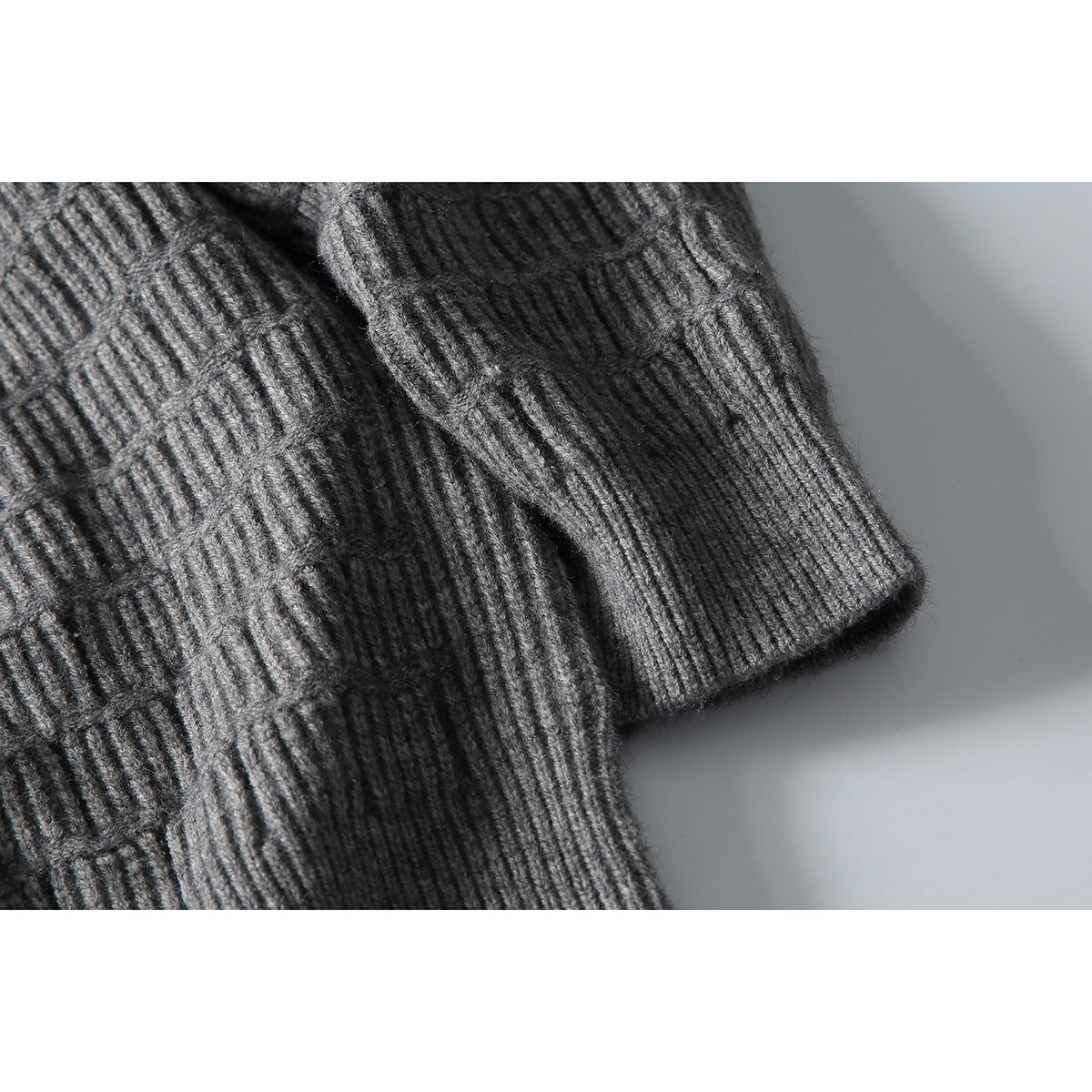 Close-up of a gray knit sweater showing its ribbed sleeve cuff and raised stitch pattern.