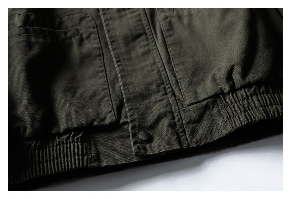 Close-up of a dark olive jacket's front snap placket, pocket edge, and gathered hem.