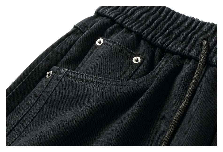 Close-up of a front pocket, metal rivets, gathered waistband, and drawstring on black pants.