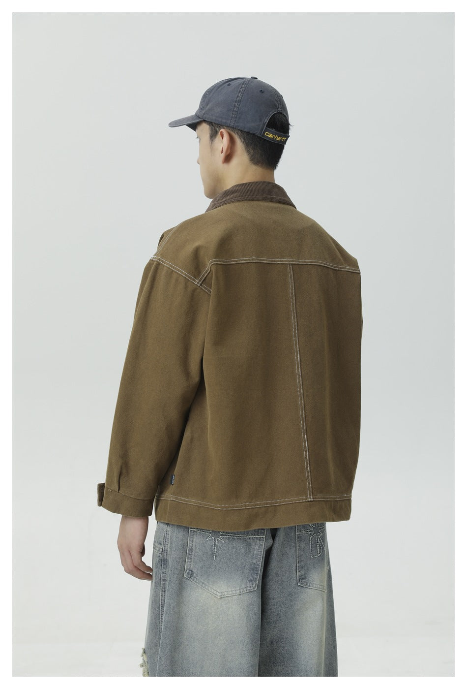 Back view of a man wearing olive brown work jacket with contrast stitching on the back yoke and center seam