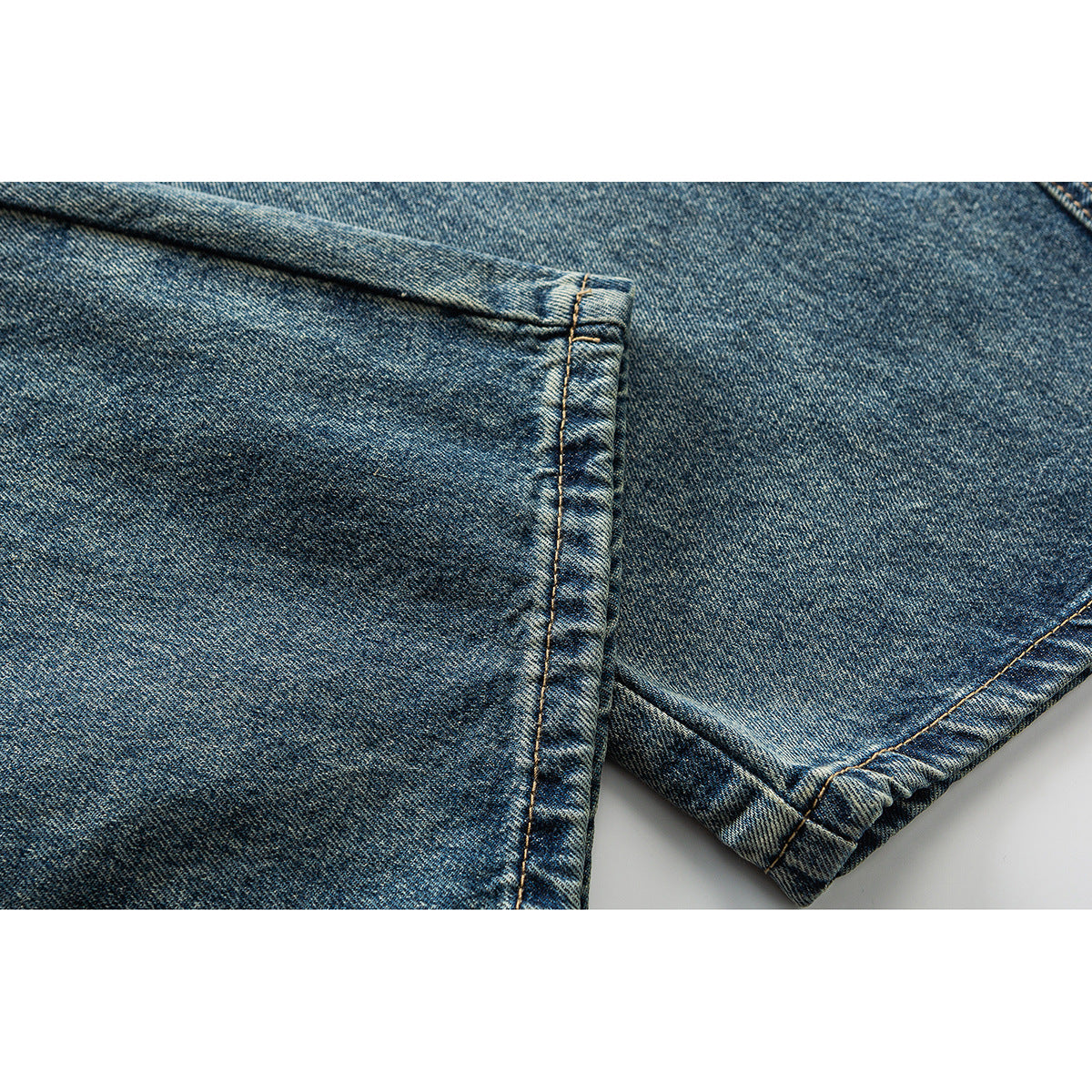 Close-up of faded blue denim leg hems, showing folded edges and contrast stitching.