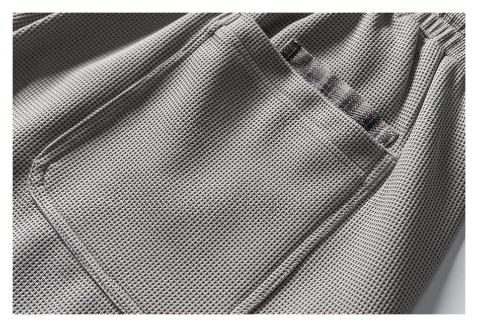 Close-up of a large pocket on gray waffle-textured shorts, edged with brown plaid trim.