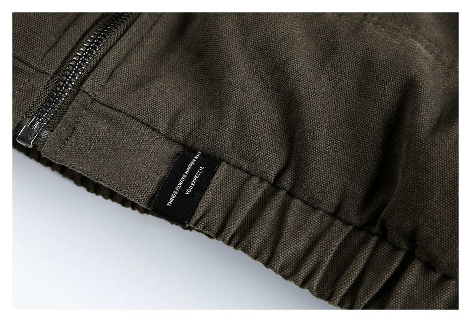 Close-up of the olive-brown jacket hem, zipper, gathered edge, and small black sewn label.