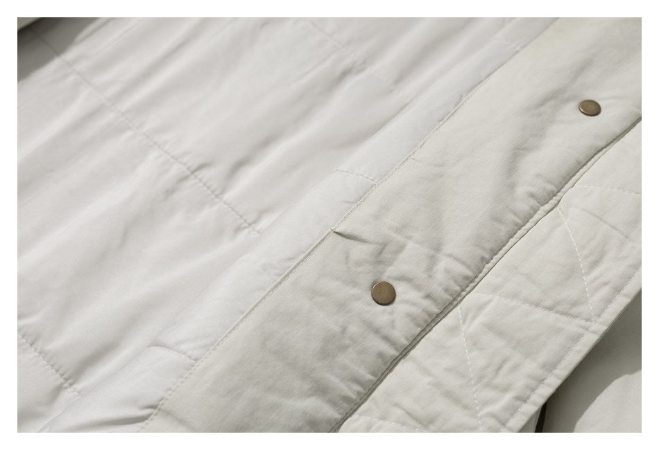 Close-up of an off-white jacket with quilted lining and metal snap fasteners.