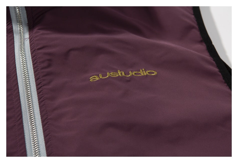 Close-up of gold embroidered lettering on the burgundy vest beside a silver zipper.